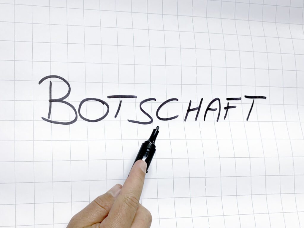 Nahaufnahme einer Flipchart mit Schriftzug Botschaft und einer Hand unten, die einen schwarzen Permanent-Marker hält und auf das "C" im Schriftzug zeigt
